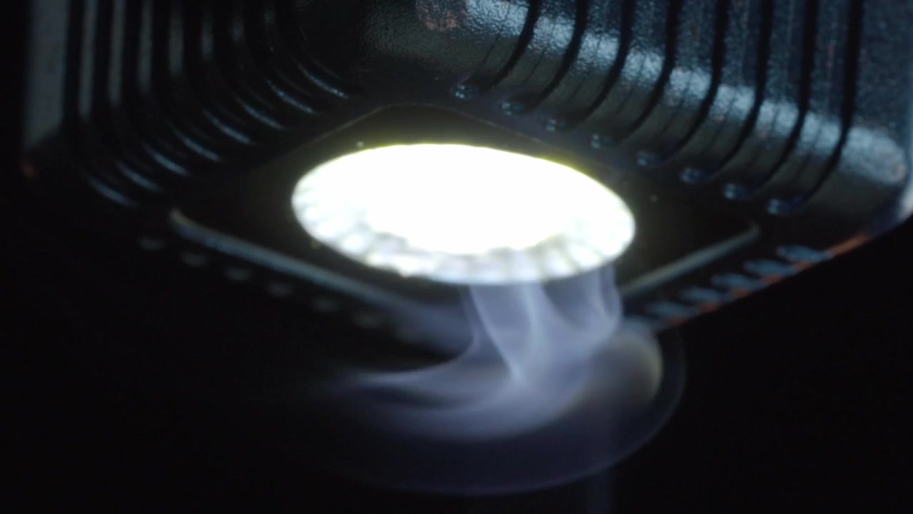 Makroaufnahme von aufsteigendem Zigarrenrauch unter hellem LED-Licht, der durchscheinenden Dampf, schwebende Bewegung und beleuchtete Rauchschwaden vor dunklem Hintergrund hervorhebt.