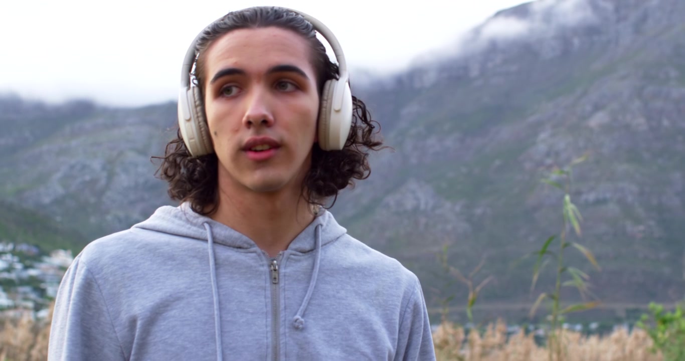 Uomo adulto che controlla lo smartwatch, reagisce a un avviso e osserva le montagne in riva al lago con le cuffie.