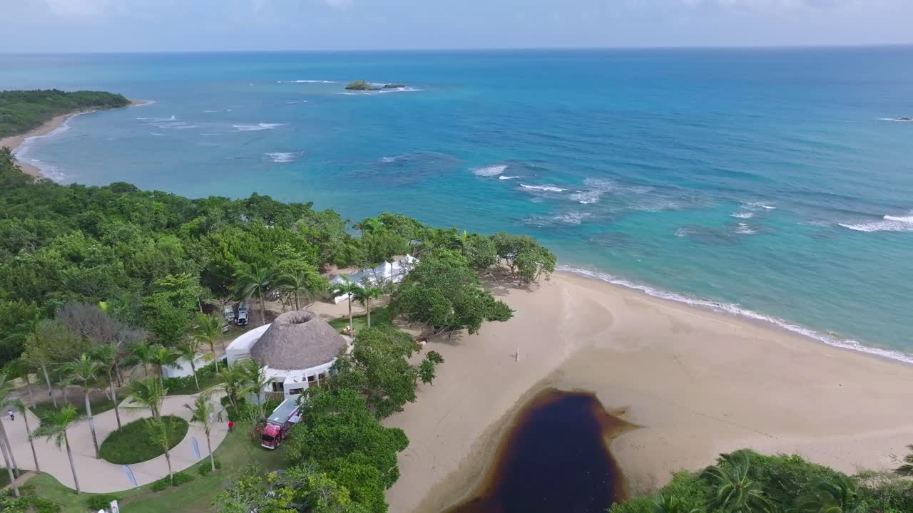 órbita aérea alrededor de un complejo tropical con palmeras y una gran costa de playa de arena