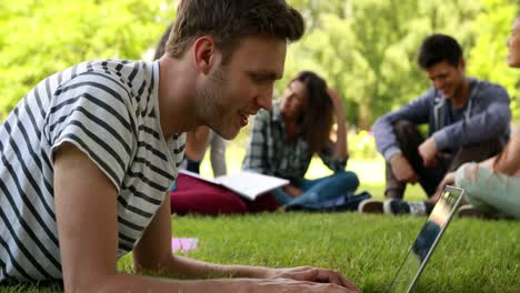 student using laptop and classmates speaking behind him