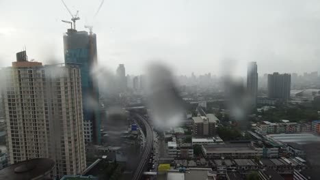 rain drop on window. aerial view. raining outside living room window on rainy season in bangkok thailand. outside window is blurred of raining city building and road and sky.