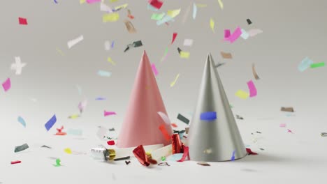 Video-of-a-pink-and-a-silver-party-hat-with-colourful-confetti-falling-on-pale-grey-background