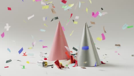 video of a pink and a silver party hat with colourful confetti falling on pale grey background