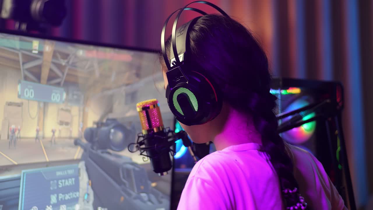 vista de cerca de atrás de una chica asiática que se estira mientras juega un juego a través de la red en una computadora personal. videojuego de transmisión en vivo, escritorio iluminado por luz de tira led rgb