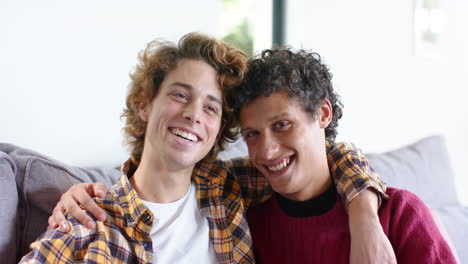 Portrait-of-happy-diverse-gay-male-couple-embracing-on-sofa-at-home,-slow-motion