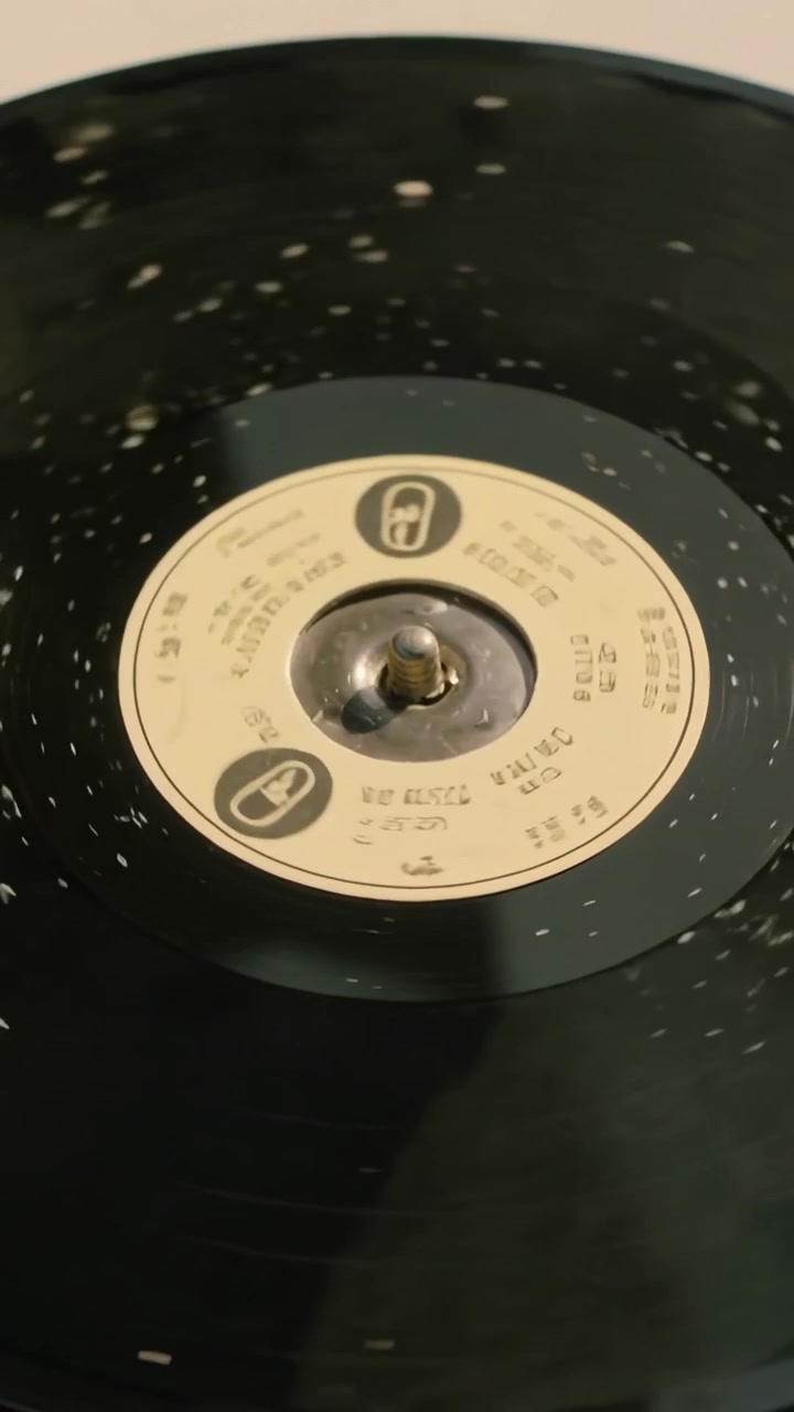 Video verticale: Vinile che gira sul perno del giradischi, con la telecamera che esegue una panoramica per mostrare l'etichetta beige e le macchioline.