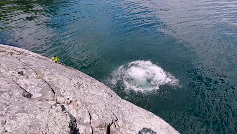 Un-Joven-Blanco-Salta-De-Un-Acantilado-Rocoso-Al-Lago-Azul-En-Cámara-Lenta,-Con-Una-Amplia-Panorámica-Sobre-La-Cabeza