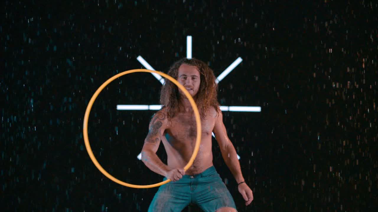 Caucasian male hula hooper playing with hula hoop in wet rain studio