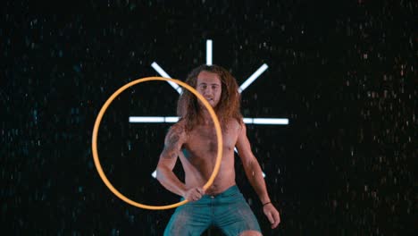 caucasian male hula hooper playing with hula hoop in wet rain studio