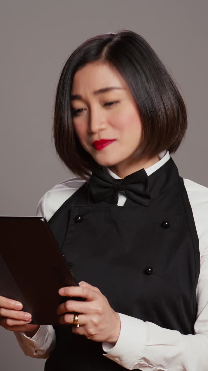 Vertikal video: Asiatisk restaurant tjener tjekker alle bordreservationer på tablet