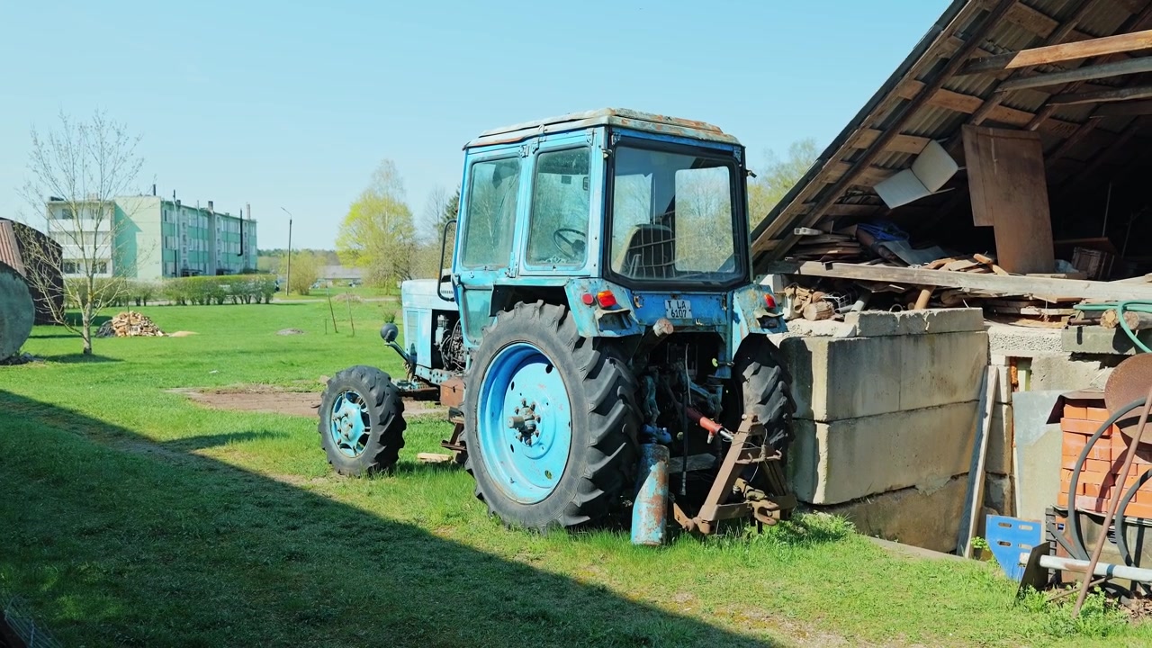 Old MTZ Belarus tractor stands near farm shed in post Soviet rural landscape