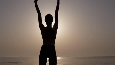 Stunning-backside-view-of-a-slender,-fit-girl-standing-against-the-sea.-Meets-morning-sunrise.-Strong-and-aspiring