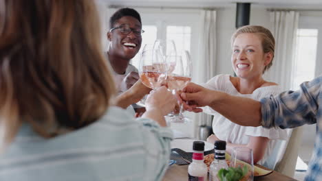 group of young friends sitting around table making a toast before enjoying meal together