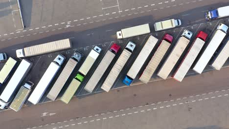 Aerial-Shot-of-Truck-with-Attached-Semi-Trailer-Leaving-Industrial-Warehouse-Storage-Building-Loading-Area-where-Many-Trucks-Are-Loading-Unloading-Merchandise