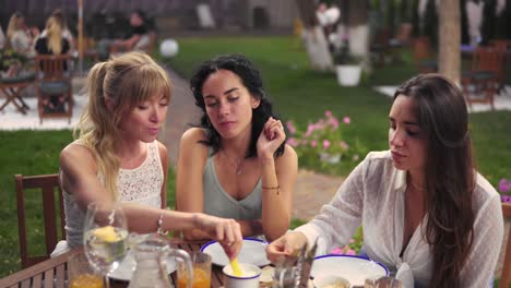 Three-Cheerful-Women-Resting-Talking-Drinking,-Eating-In-Summer-Veranda-Cafe-Casual-City-Friendship-Models-Outdoors