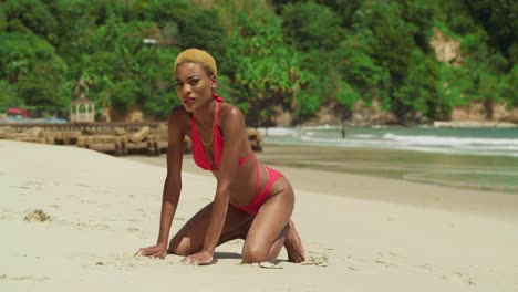 on the pristine shores of a caribbean beach, a girl with dark skin stands out in a red bikini kneel in the sand