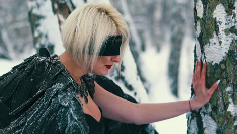mujer en traje de fénix con los ojos vendados se inclina sobre un árbol en el bosque
