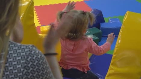 young mother and daughter are playing in the playroom climbing on an inflatable hill