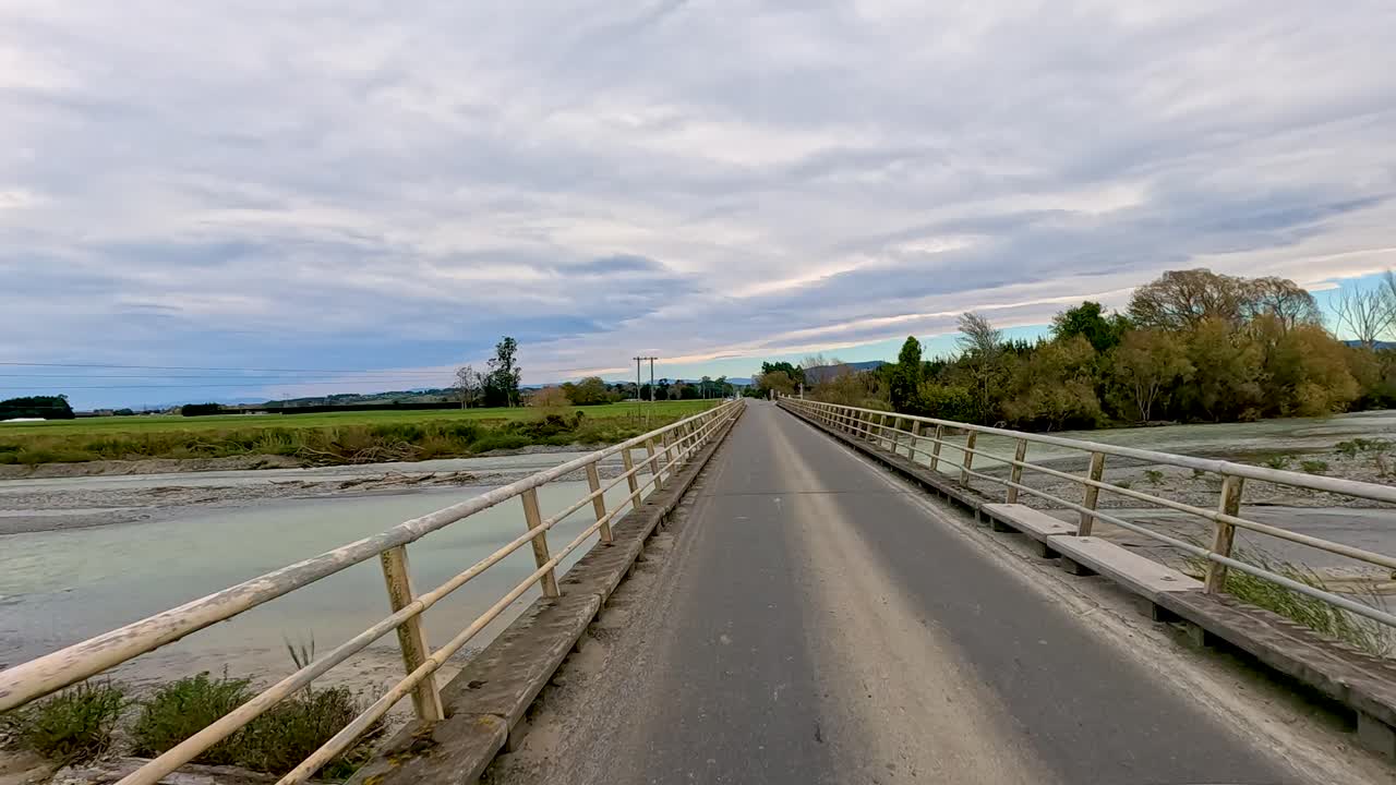 A serene drive over a bridge at Lake Tekapo, showcasing expansive landscapes under cloudy skies with a tranquil atmosphere