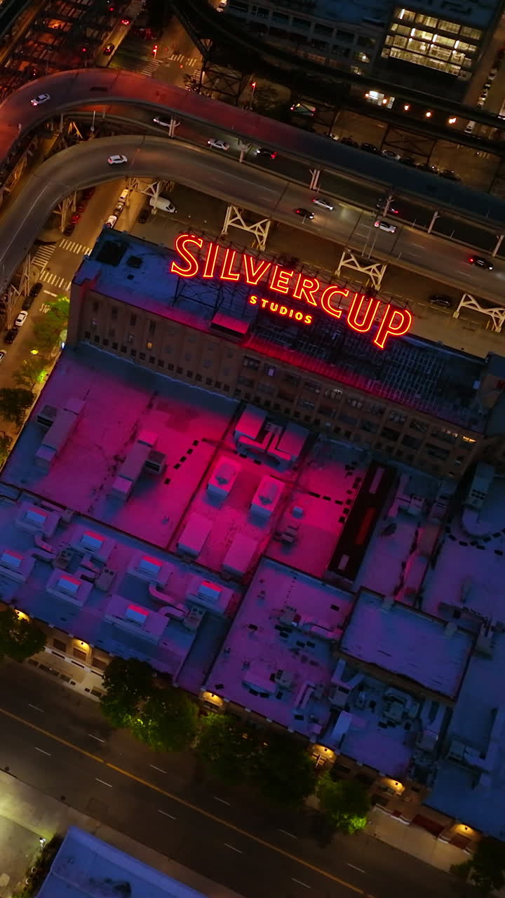 Silvercup Studios surrounded by roads with lively traffic at night time. Top view on the roofs of buildings with gradual descending. Vertical video