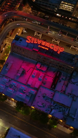 silvercup studios surrounded by roads with lively traffic at night time. top view on the roofs of buildings with gradual descending. vertical video