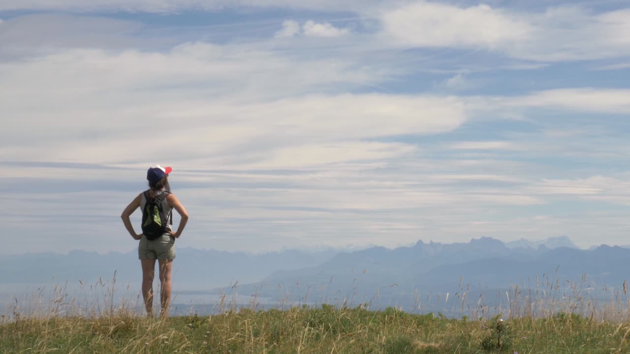 una excursionista solitaria se encuentra en la cima de una montaña mirando la vista de un gran lago alpino y los picos alpinos circundantes