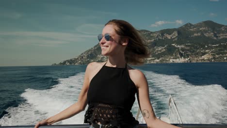 lovely caucasian girl standing on a moving yacht with water trail and mountain background in italy