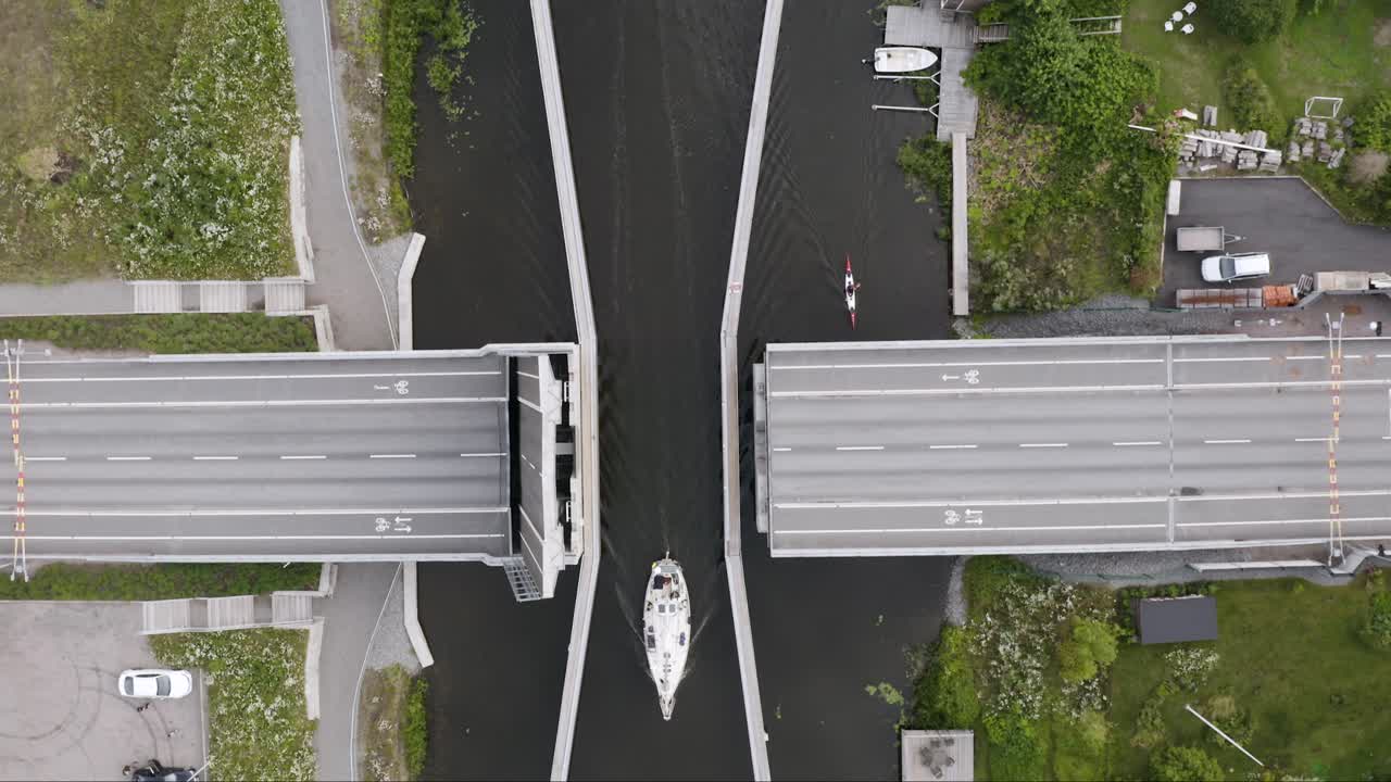 Overhead aerial of sailboat passing road bridge in canal