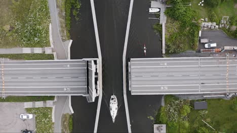 overhead aerial of sailboat passing road bridge in canal