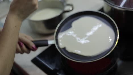 The-process-of-cooking-homemade-pancakes.-Woman-pours-pancake-dough-on-pan