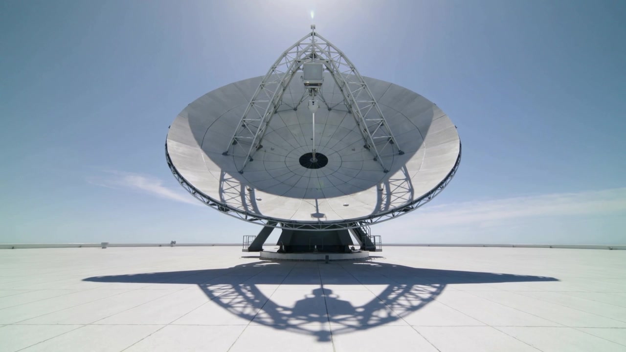 Skiftende sollys får en parabolantenne til at kaste en langsom skygge på et tegltag, med gitterarme