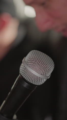 primer plano de un micrófono en foco con un fondo borroso con la mano de un hombre y parte de su cara. la escena sugiere un entorno de estudio, posiblemente durante una sesión de grabación