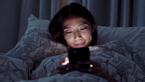 woman using phone in bed at night