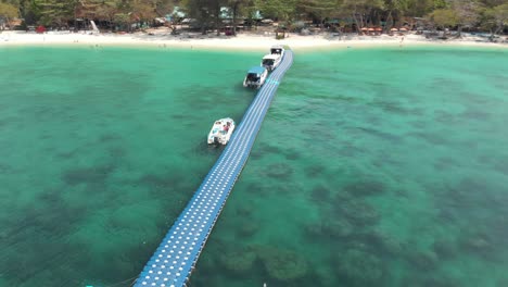 floating pier with moored tourist tour boats in the idyllic emerald water of banana beach, koh hey , thailand - aerial low-angle orbit shot