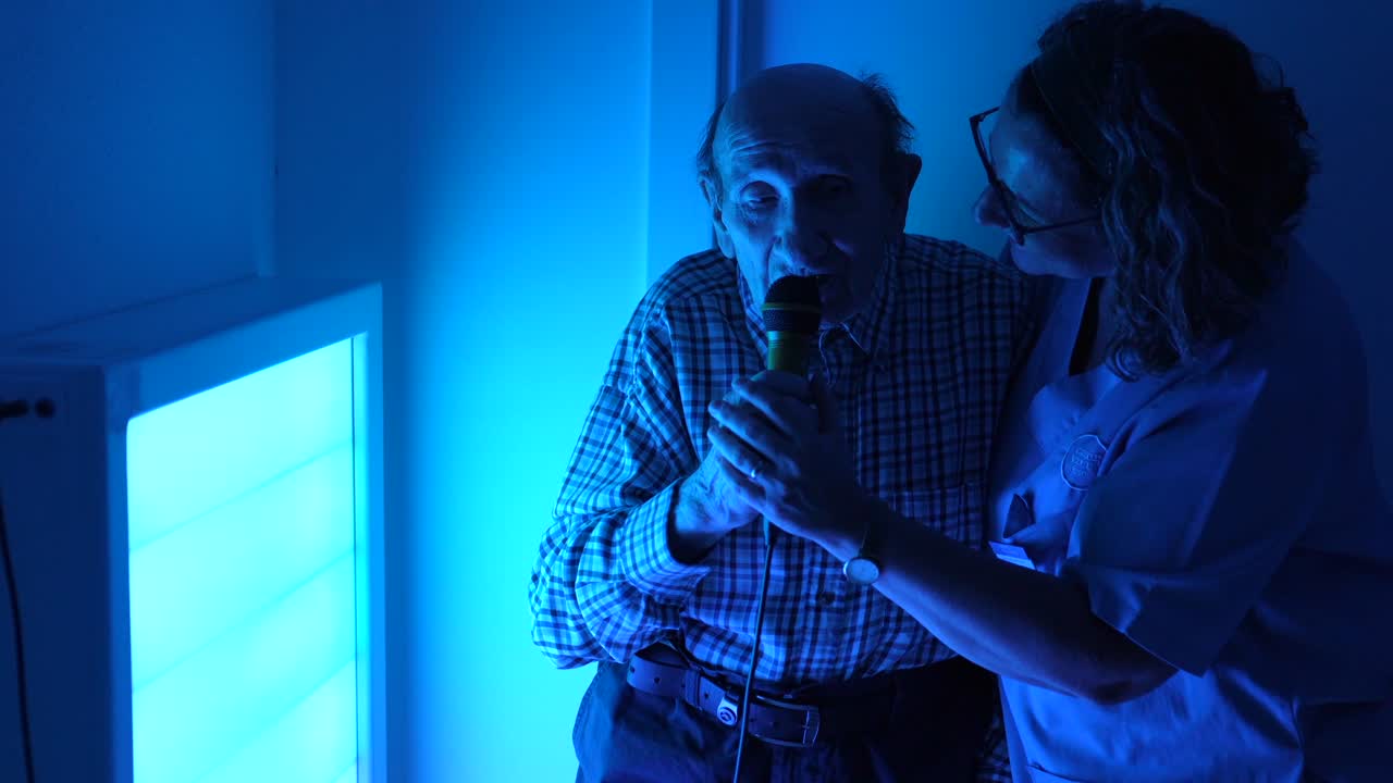 Elderly man singing with caregiver in blue light therapy setting