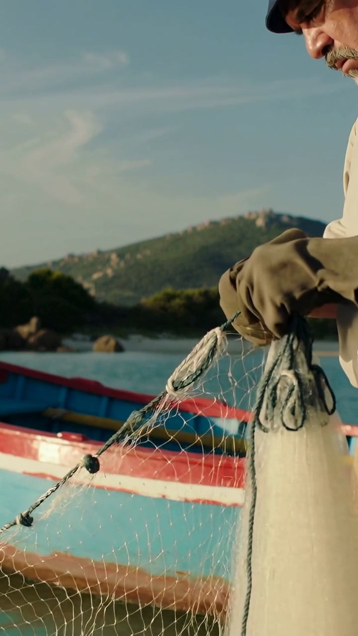 Vertical video: Inspecting net, fisher mending knots at cove by boat with gloved hands, copy space