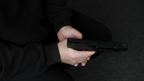 a man loading and cocking a pistol hand gun while sitting down