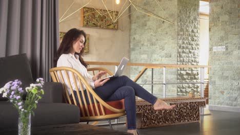 mujer de negocios se sienta en la silla en su casa de lujo y usando una computadora portátil para trabajar desde casa temprano en la mañana, mujer usuario profesional usando tecnología haciendo trabajo remoto en línea en casa