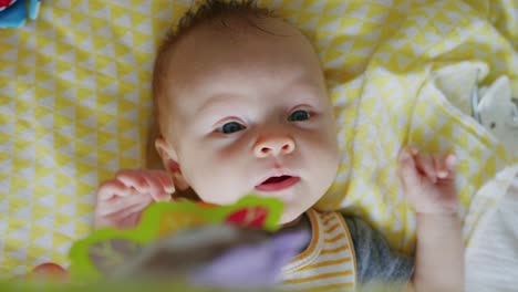 adorable baby laughs and giggles while playing under her hanging toys on a yellow blanket