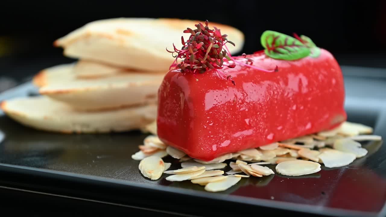 Dessert servert på svart tallerken med mandelbiter og fruktdekorasjon. Rød dessert er plassert på en svart tallerken med mandelbiter og fruktdekorasjoner