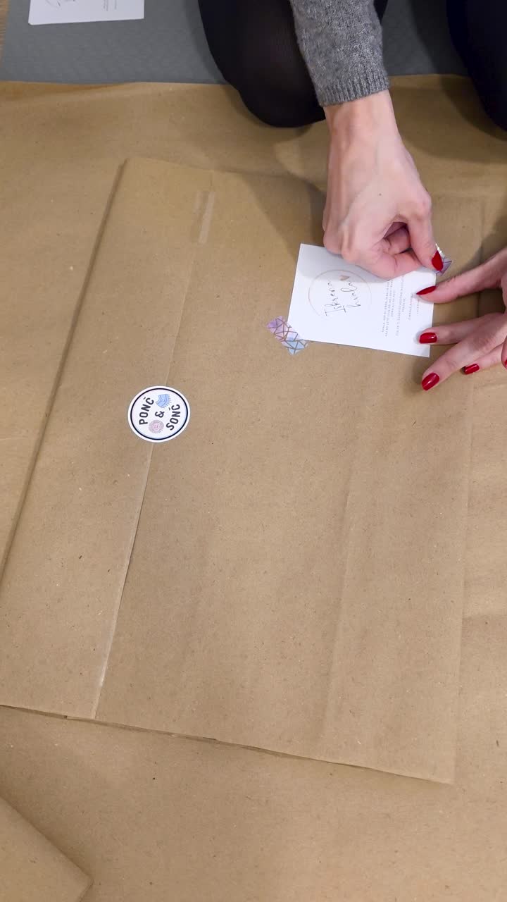 Hands wrap a corporate gift in kraft paper with label and seal - gifting business partners at christmas time, Vertical close-up handheld shot