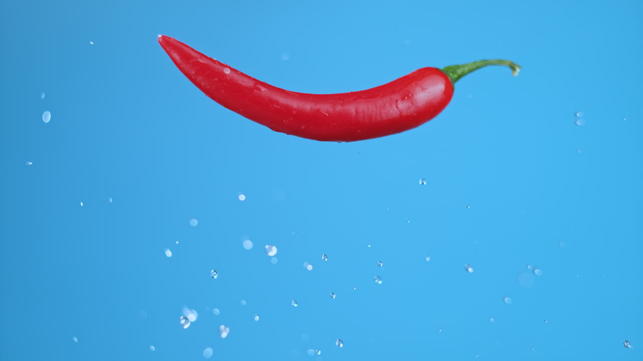 빨간 뜨거운 칠리 고추가 날아오르고, 점프하고 수평으로 머물며, 물방울이 있습니다.