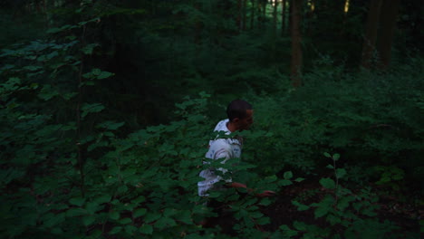 young man with short hair is walking on a small path in a dark forest