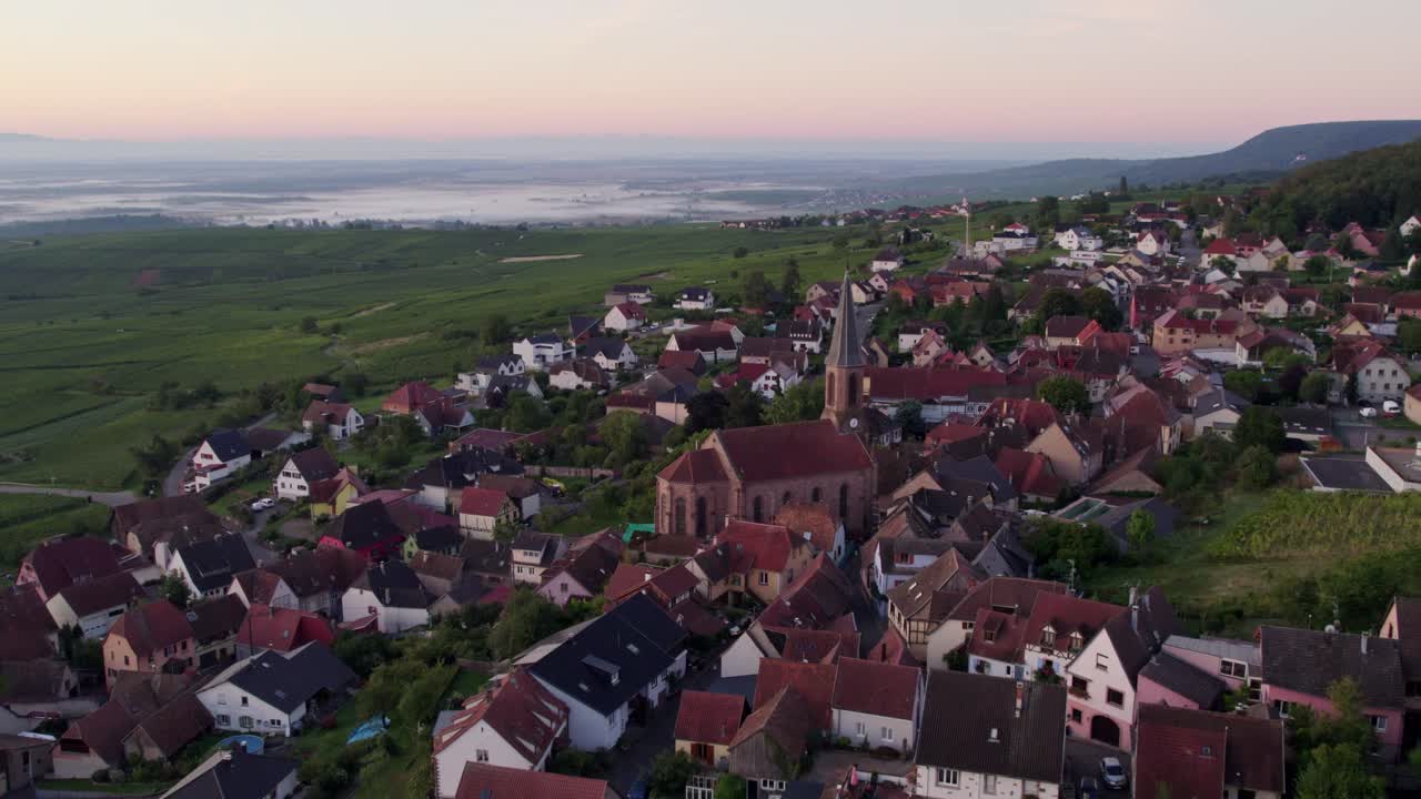 Wschód słońca nad winnicą i kościołem w Husseren-les-Chateaux