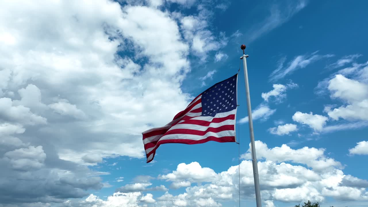 La bandiera americana degli Stati Uniti sventola contro un cielo limpido e soleggiato con nuvole bianche e gonfie.