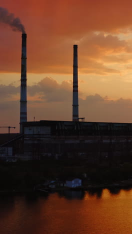 factory on orange background. harmful chemical plant over the river at sunset. large territory of industrial plant in the countryside. vertical video