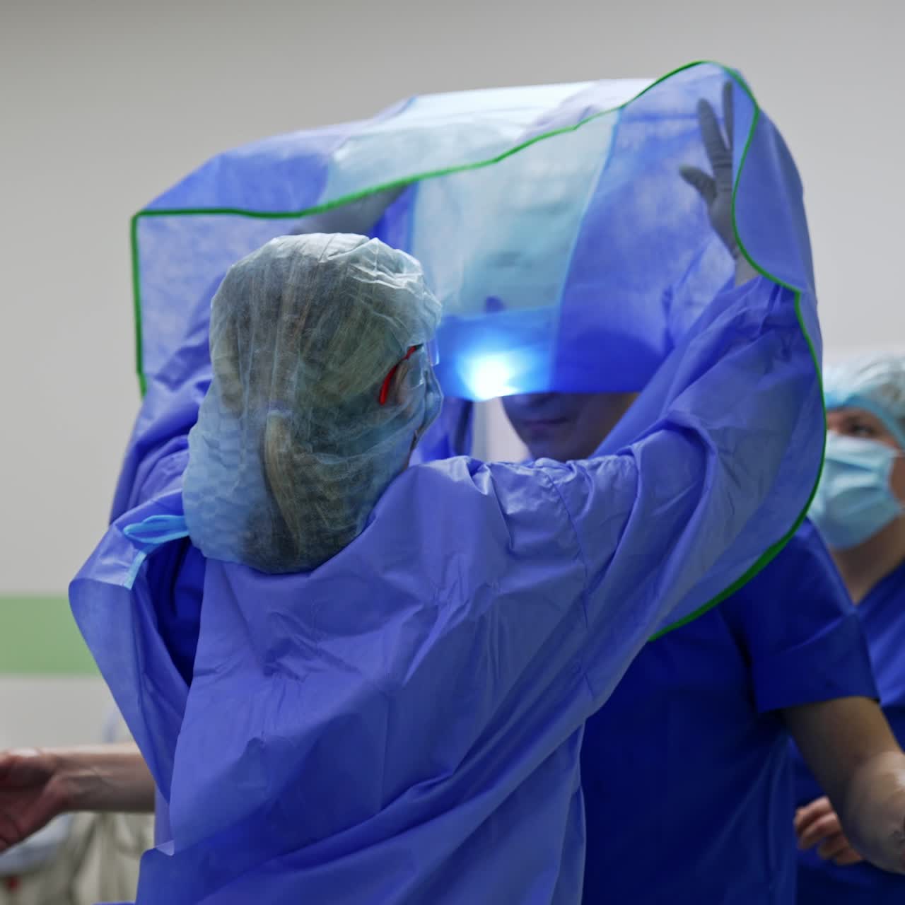 Nurses put on the protective suit on a main surgeon. Medical personnel preparing the doctor for surgical procedure
