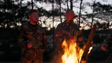 conversation of soldiers in camouflage clothes, they are discussing in the evening by the common bonfire frying sausages for supper, men are resting after work, service, field exercises