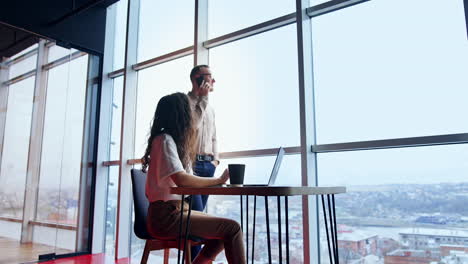 office with panoramic windows and people working there. male employee speaks on the phone and woman works at laptop. low angle view.