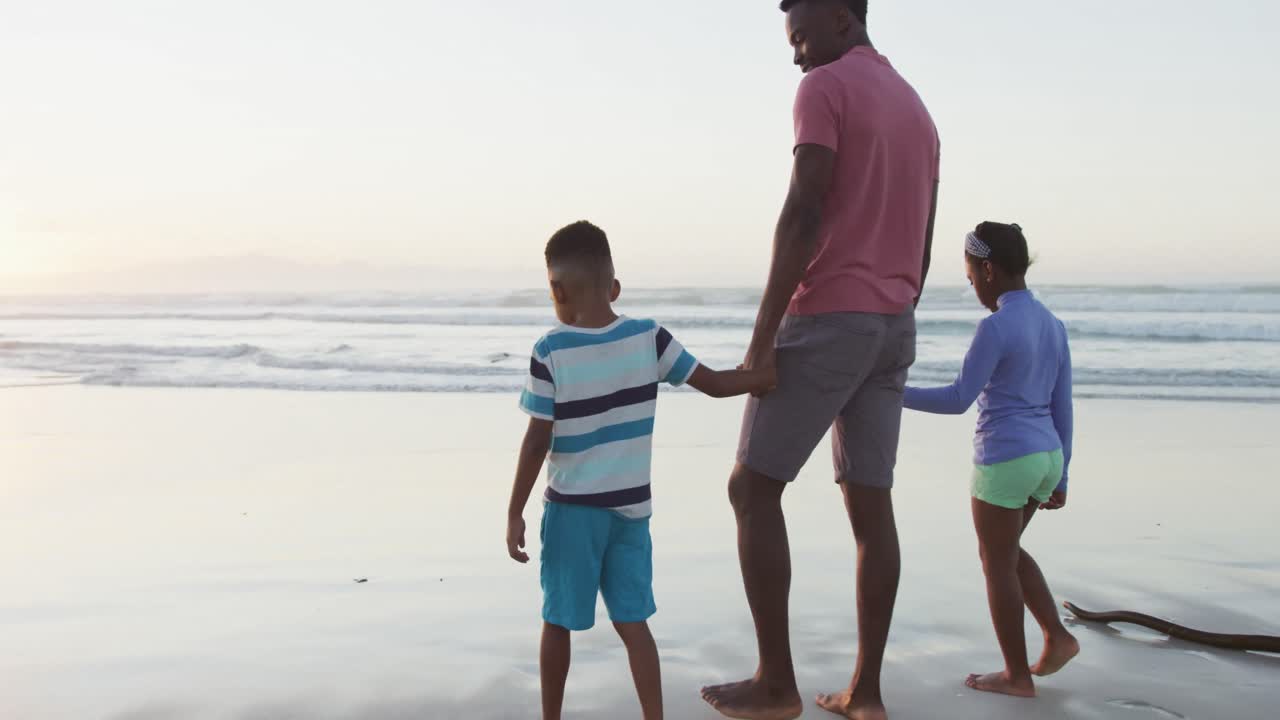 Padre afroamericano che cammina con la figlia e il figlio su una spiaggia soleggiata